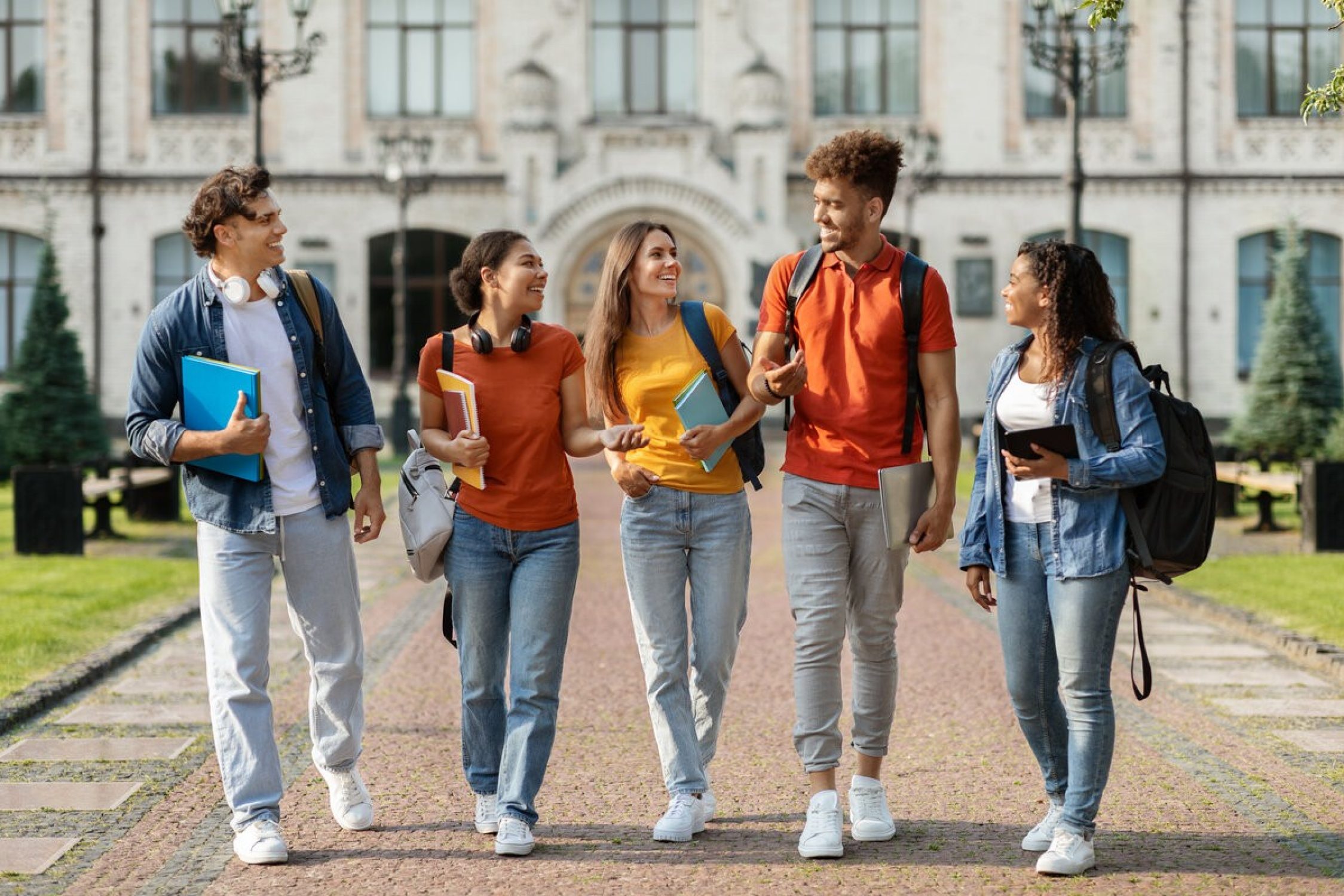 Eine Gruppe internationaler Studierende laufen zusammen durch den Campus und halten Bücher in den Händen.